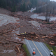 An aerial look at a debris flow that crosses a road as a crew of workers looks at the damage.